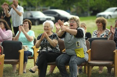 İnsanlar köy gününe adanmış konser sırasında kırsal bir çimenlikteki banklarda oturuyorlar. 12 Haziran 2021. Borysivka, Ukrayna