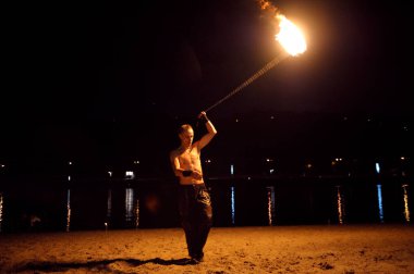 Man fire juggler performing with burning torches at night on a sandy beach. November 11, 2019. Kiev, Ukraine clipart