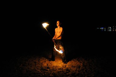 Ateş hokkabazı, kumlu bir sahilde geceleri yanan meşalelerle gösteri yapıyor. 11 Kasım 2019. Kiev, Ukrayna