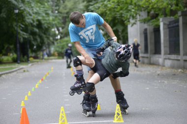 Paten kaymak. Antrenör, ona sanatsal slalom öğretirken küçük çocukla oynaşıyor. 25 Haziran 2019. Kyiv, Ukrayna