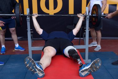 Spor salonunda halter kaldıran özel ihtiyaçları olan erkek sporcu, diğer erkekler yardım ediyor. 25 Haziran 2019. Kyiv, Ukrayna