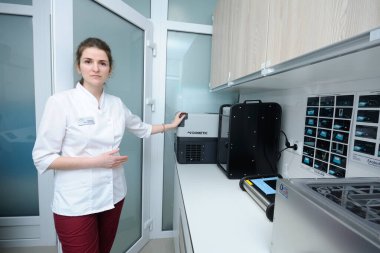 At the Human Milk Bank laboratory. Lab assistant standing near table with milk heating box, freezer and milk analizer and telling about it. April 12, 2019. Kiev, Ukraine clipart