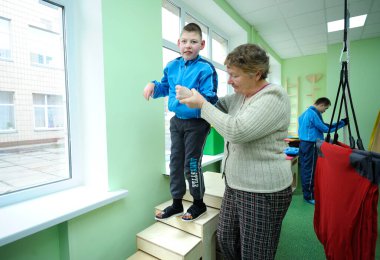 Hareket kontrolünün geliştirilmesi: Down sendromlu çocuğun rehabilitasyon odasında egzersiz yapmasına yardım eden kadın terapist. 12 Şubat 2019. Kiev, Ukrayna