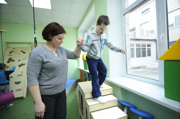 Hareket kontrolünün geliştirilmesi: Down sendromlu çocuğun rehabilitasyon odasında egzersiz yapmasına yardım eden kadın terapist. 12 Şubat 2019. Kiev, Ukrayna