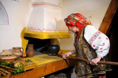 Ukrayna yerlisi kostümlü bir kadın geleneksel aletli otları kırsal bir fırına koyuyor, klasik kırsal eve. 23 Mart 2018. Kyiv, Ukrayna