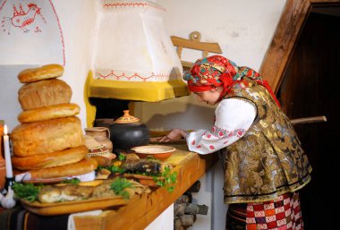 Ukrayna yerlisi kostümlü bir kadın geleneksel aletli otları kırsal bir fırına koyuyor, klasik kırsal eve. 23 Mart 2018. Kyiv, Ukrayna