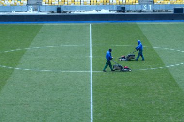 İşçiler çim biçme makinesi kullanarak futbol sahasında çim biçiyor. 16 Mart 2018. Kyiv, Ukrayna