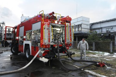 Kurtarma ekibi kimyasal arındırma eğitimi alıyor: itfaiye aracı park halinde, yangın musluklarına bağlı hortumlar, arka planda fabrika tesisi. 21 Şubat 2019. Kiev, Ukrayna