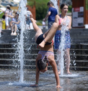 Küçük kız fıskiyelerin önünde amuda kalkarak akrobatik numaralar yapıyor. 15 Haziran 2021. Kyiv, Ukrayna