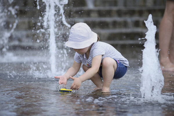 Little girl playing with fountain water jets, summer strong heat in the city. June 15, 2021. Kyiv, Ukraine