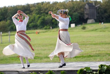Ulusal Letonya kostümlü iki genç kadın yaz ortasında Jan Day 'i kutlayarak dans ediyorlar. Letonya Kültürü Günleri. 18 Haziran 2021. Pyrogove, Kyiv, Ukrayna