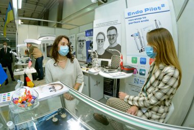 Young women managers sitting behind the stand presenting medical instruments. Expodental exhibition. November 25, 2020. Kiev, Ukraine clipart