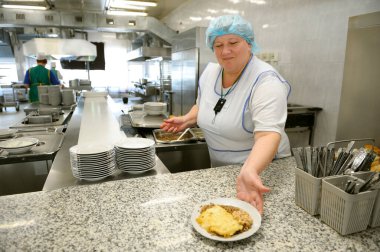 At the canteen of Chernobyl Nuclear Power Plant. Cook preparing dish for customers to put it on a canteen counter. April 20, 2018. Chernobyl, Ukraine clipart