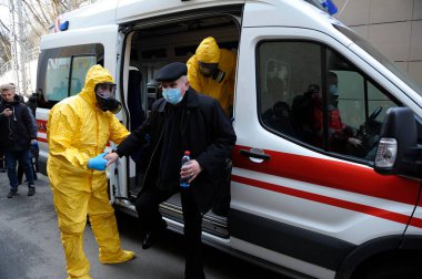 Sağlık görevlileri maskeli yaşlı bir adama ambulans arabasından enfeksiyon hastalıkları departmanına, koronavirüse gitmesi için yardım ediyor. 26 Şubat 2020. Kiev, Ukrayna
