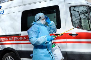 Sağlık görevlileri ambulans arabasını motorlu sırt çantası atomizleyicisi ve spreyiyle dezenfekte ediyorlar.