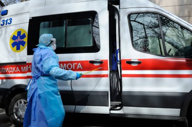 Sağlık görevlileri ambulans arabasını motorlu sırt çantası atomizleyicisi ve spreyiyle dezenfekte ediyorlar.