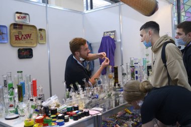 Seller showing equipment for smoking marijuana to young people at the cannabis shop. Cannabis fair. October 2, 2020. Kyiv, Ukraine clipart