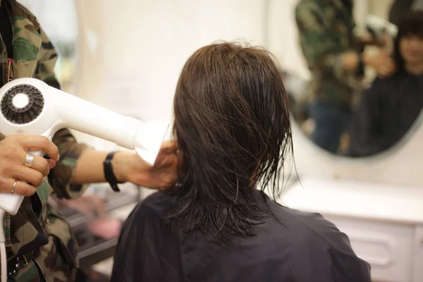 Male hairdresser applying a hair dryer to a woman\'s hair