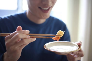 Karides yiyen bir adam tempura kuyruğu yiyor