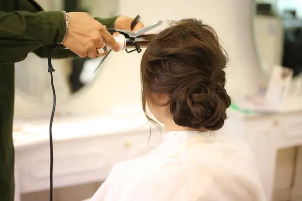 Male hairdresser applying curling iron to woman\'s hair
