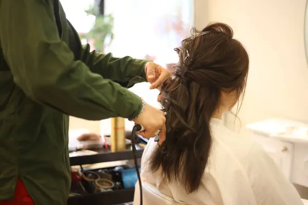 Male hairdresser applying curling iron to woman's hair