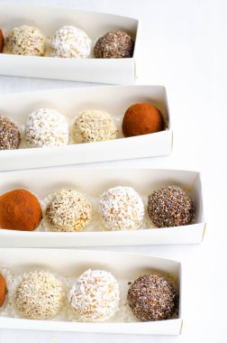 Çeşitli vejetaryen tatlılar, tohumlu lezzetli şeker topları, kurutulmuş meyve ve kakao tozu, Chia 'lı sağlıklı şeker, susam tohumları, Hindistan cevizi ve mantarlar parlak arkaplanda karton kutularda.