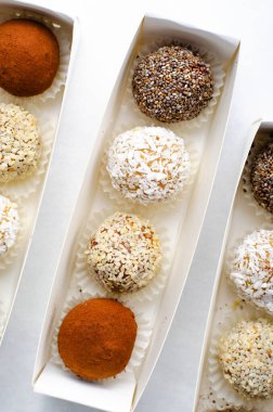 Çeşitli vejetaryen tatlılar, tohumlu lezzetli şeker topları, kurutulmuş meyve ve kakao tozu, Chia 'lı sağlıklı şeker, susam tohumları, Hindistan cevizi ve mantarlar parlak arkaplanda karton kutularda.