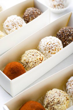 Çeşitli vejetaryen tatlılar, tohumlu lezzetli şeker topları, kurutulmuş meyve ve kakao tozu, Chia 'lı sağlıklı şeker, susam tohumları, Hindistan cevizi ve mantarlar parlak arkaplanda karton kutularda.