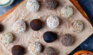 Assorted vegan sweets, Delicious Candy Balls with seeds, dried fruit, nuts, and cocoa powder, Healthy Candies with Chia, Sesame Seeds, Coconut and Truffles on wooden background