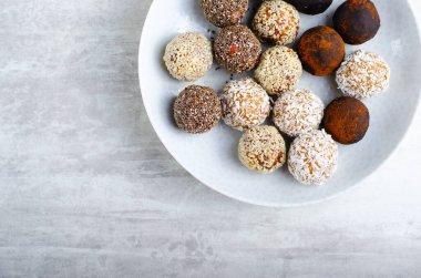 Assorted vegan sweets, Delicious Candy Balls with seeds, dried fruit and cocoa powder, Healthy Candies with Chia, Sesame Seeds, Coconut and Truffles on a Plate on grey background