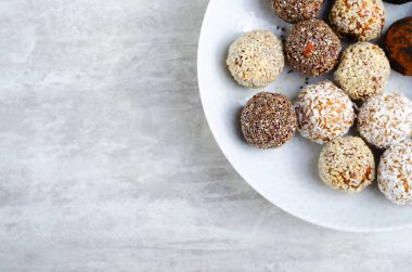 Assorted vegan sweets, Delicious Candy Balls with seeds, dried fruit and cocoa powder, Healthy Candies with Chia, Sesame Seeds, Coconut and Truffles on a Plate on grey background