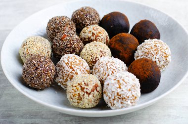 Assorted vegan sweets, Delicious Candy Balls with seeds, dried fruit and cocoa powder, Healthy Candies with Chia, Sesame Seeds, Coconut and Truffles on a Plate on grey background