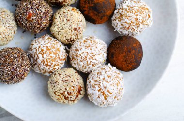 Assorted vegan sweets, Delicious Candy Balls with seeds, dried fruit and cocoa powder, Healthy Candies with Chia, Sesame Seeds, Coconut and Truffles on a Plate on grey background