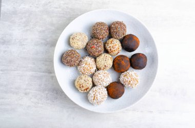 Assorted vegan sweets, Delicious Candy Balls with seeds, dried fruit and cocoa powder, Healthy Candies with Chia, Sesame Seeds, Coconut and Truffles on a Plate on grey background