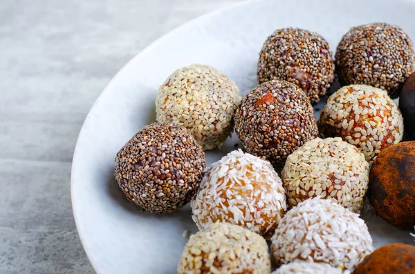 Assorted vegan sweets, Delicious Candy Balls with seeds, dried fruit and cocoa powder, Healthy Candies with Chia, Sesame Seeds, Coconut and Truffles on a Plate on grey background