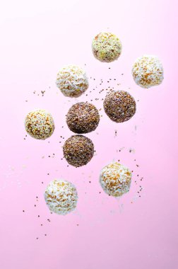 Levitating Assorted Vegan Sweets, Delicious Candy Balls with seeds, dried fruit, Healthy Candies with Chia, Sesame Seeds, and Coconut on Pink background