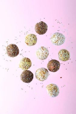 Levitating Assorted Vegan Sweets, Delicious Candy Balls with seeds, dried fruit, Healthy Candies with Chia, Sesame Seeds, and Coconut on Pink background