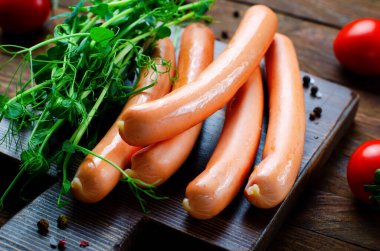 Classic Sausages on Wooden Board with herbs and cherry tomatoes on dark background, Snack