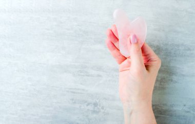 Rose Quartz Gua Sha tool in Woman Hands, Facial Lifting Scraping Massage Treatment