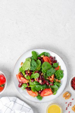 Kırmızı fasulye salatası, ıspanaklı vegan salatası, vişneli domates, ceviz, fasulye ve parlak arkaplanda hardal sosu.