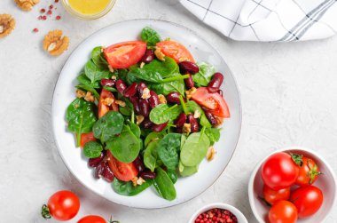 Kırmızı fasulye salatası, ıspanaklı vegan salatası, vişneli domates, ceviz, fasulye ve parlak arkaplanda hardal sosu.
