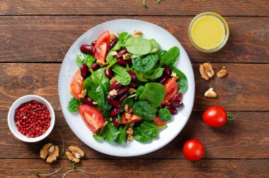 Kırmızı fasulye salatası, ıspanaklı vegan salatası, vişneli domates, ceviz, fasulye ve hardal soslu ahşap arka plan.