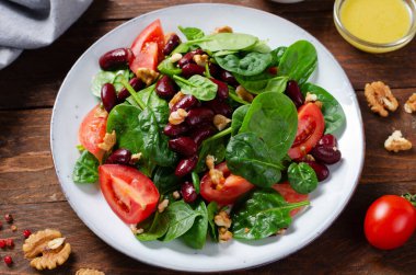 Kırmızı fasulye salatası, ıspanaklı vegan salatası, vişneli domates, ceviz, fasulye ve hardal soslu ahşap arka plan.