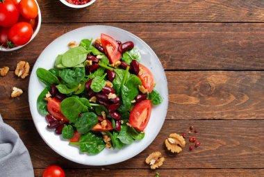 Kırmızı fasulye salatası, ıspanaklı vegan salatası, vişneli domates, ceviz, fasulye ve hardal soslu ahşap arka plan.