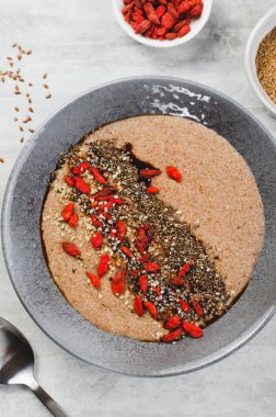 Bir kâse keten tohumu lapası, sağlıklı kahvaltı ya da atıştırmalık, Chia tohumları ve gri arkaplanda Goji meyveleriyle süslenmiş lapa.