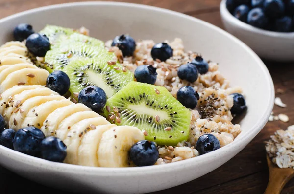 stock image Oatmeal Bowl, Oat Porridge with Blueberry, Banana and Kiwi on Dark Rustic Background, Healthy Snack or Breakfast