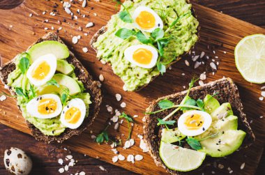 Avokado ve bıldırcın yumurtası tostları, sağlıklı atıştırmalıklar veya tahta arka planda kahvaltı.