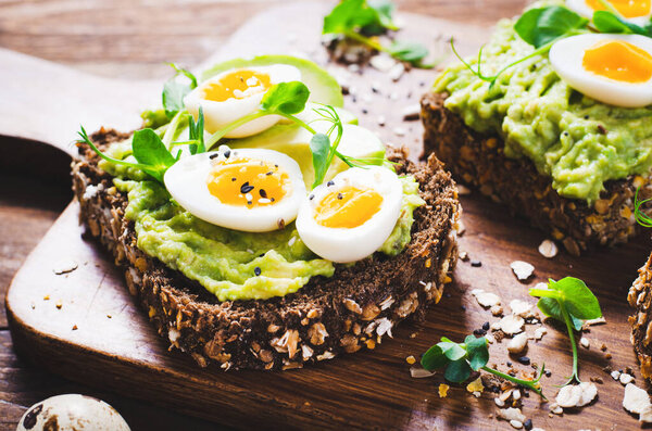 Avocado and Quail Egg Toasts, Healthy Snack or Breakfast on Wooden Background