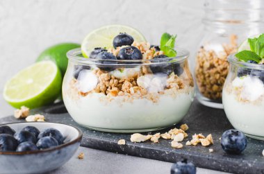 Yoğurt, kireç ve yaban mersinli gevrek, sağlıklı atıştırmalık veya Parlak Arkaplanda Kahvaltı