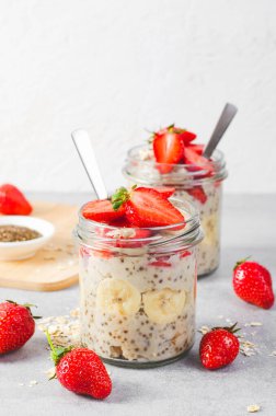 Overnight Oats with Fresh Strawberry, Banana and Chia Seeds in Jars on Grey Background, Healthy Snack or Breakfast clipart